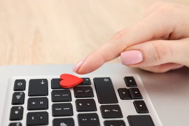 Photo of Online dating site. Woman touching red heart on laptop at table, closeup