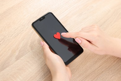 Photo of Online dating site. Woman touching red heart on smartphone at wooden table, above view