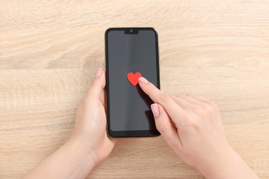 Photo of Online dating site. Woman touching red heart on smartphone at wooden table, top view
