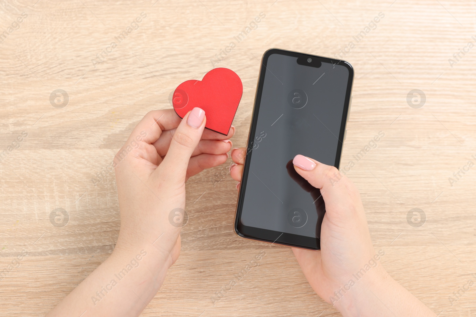 Online dating site. Woman with decorative heart and smartphone at wooden table, top view Photo of Online dating site. Woman with decorative heart and smartphone at wooden table, top view