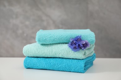 Photo of Stack of colorful towels and flowers on white table, closeup