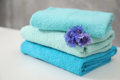 Photo of Stack of colorful towels and flowers on white table, closeup
