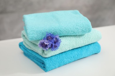 Photo of Stack of colorful towels and flowers on white table, closeup