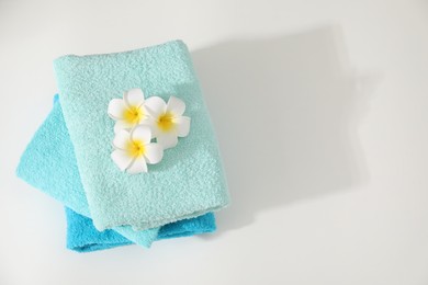 Photo of Stack of colorful towels and plumeria flowers on white table, top view. Space for text