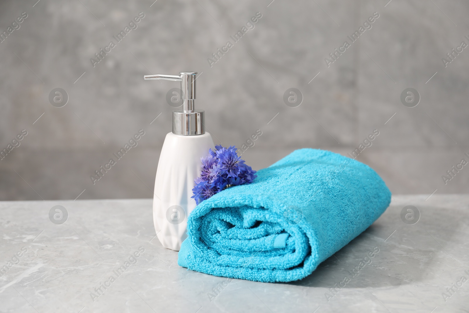 Soft towel, flowers and liquid soap on grey marble table Photo of Soft towel, flowers and liquid soap on grey marble table