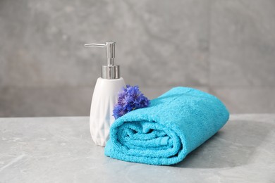 Photo of Soft towel, flowers and liquid soap on grey marble table