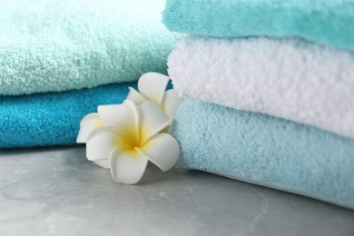 Photo of Stacks of soft towels and plumeria flowers on grey marble table, closeup