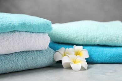 Photo of Stacks of soft towels and plumeria flowers on grey marble table, closeup