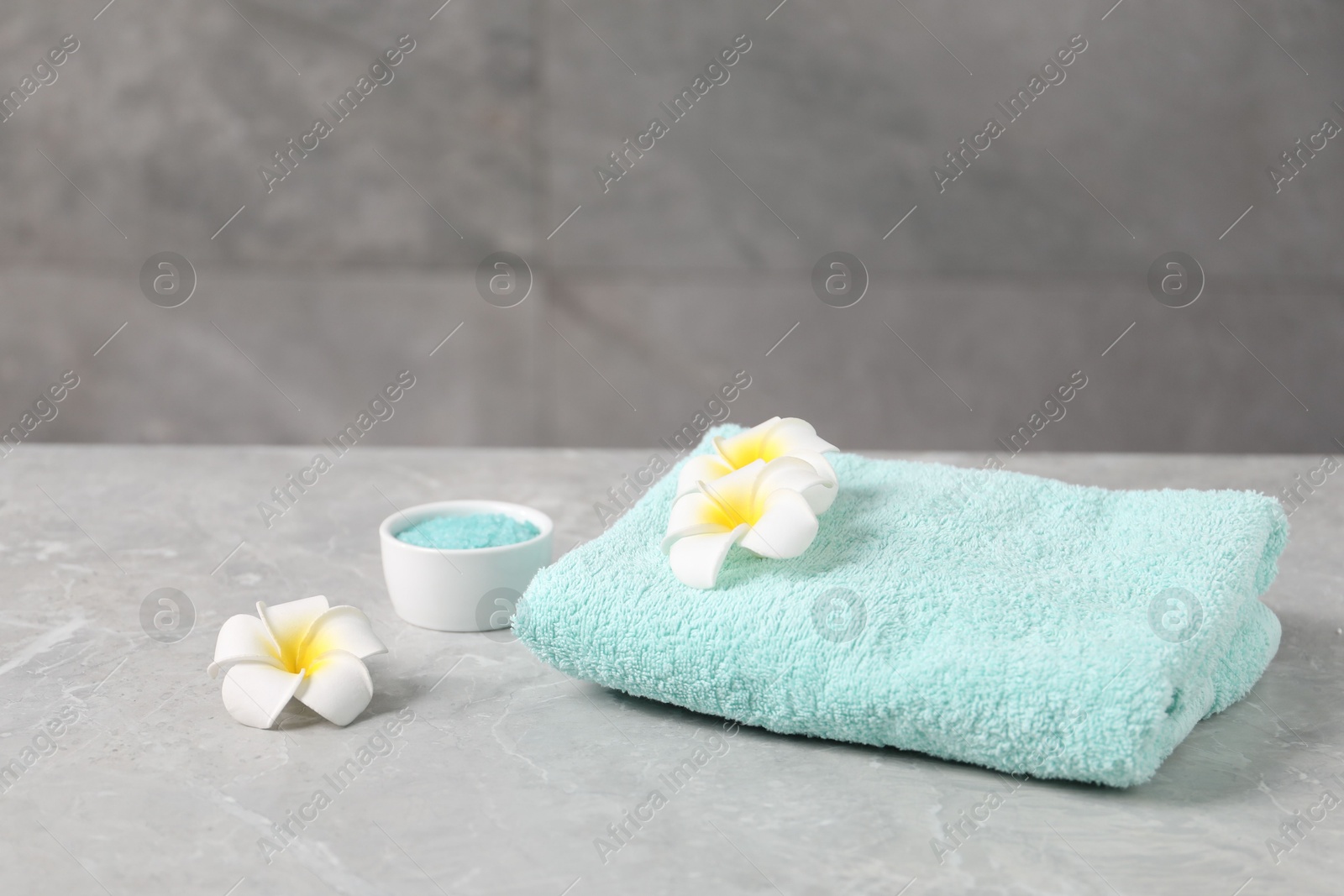 Soft towel, sea salt and plumeria flowers on grey marble table Photo of Soft towel, sea salt and plumeria flowers on grey marble table