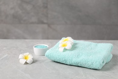 Photo of Soft towel, sea salt and plumeria flowers on grey marble table