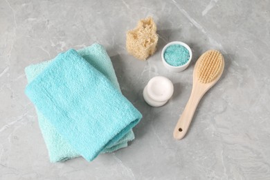 Photo of Stack of soft towels, spa stones, sea salt, loofah and brush on grey marble table, flat lay
