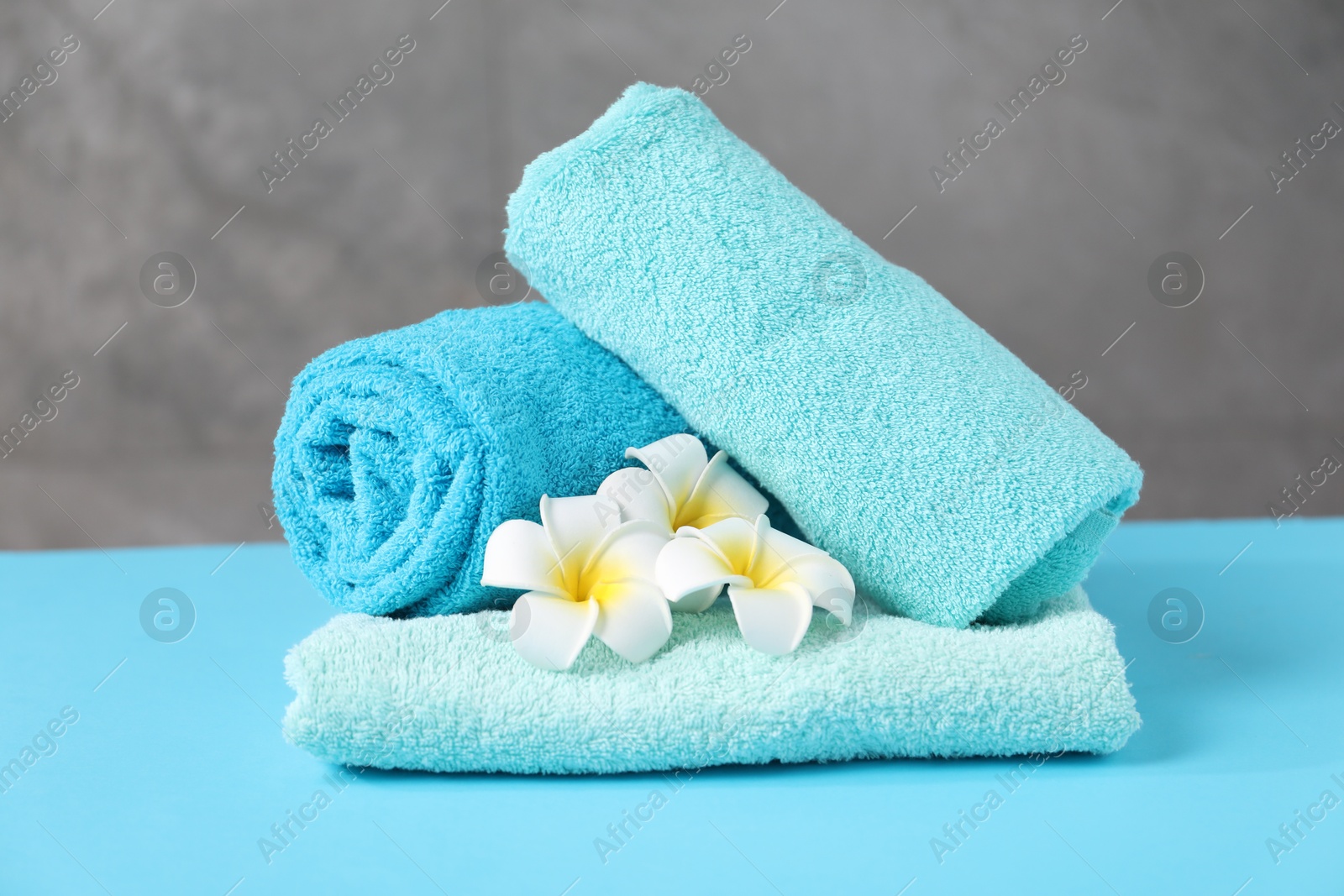 Soft towels and plumeria flowers on light blue table Photo of Soft towels and plumeria flowers on light blue table