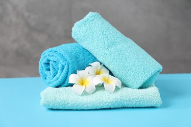 Photo of Soft towels and plumeria flowers on light blue table