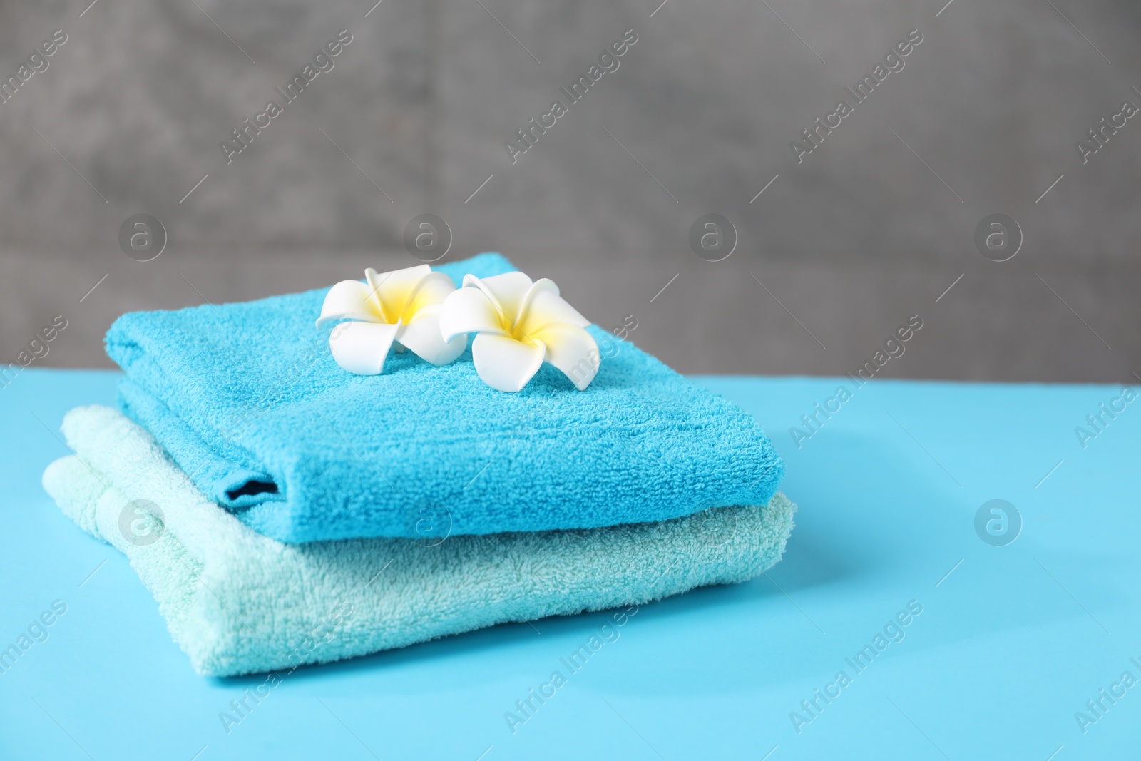 Soft towels and plumeria flowers on light blue table, closeup. Space for text Photo of Soft towels and plumeria flowers on light blue table, closeup. Space for text