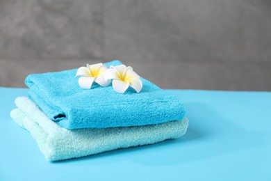 Photo of Soft towels and plumeria flowers on light blue table, closeup. Space for text