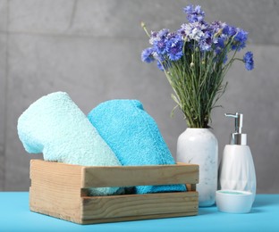 Photo of Soft towels, liquid soap, sea salt and flowers in wooden basket on light blue table