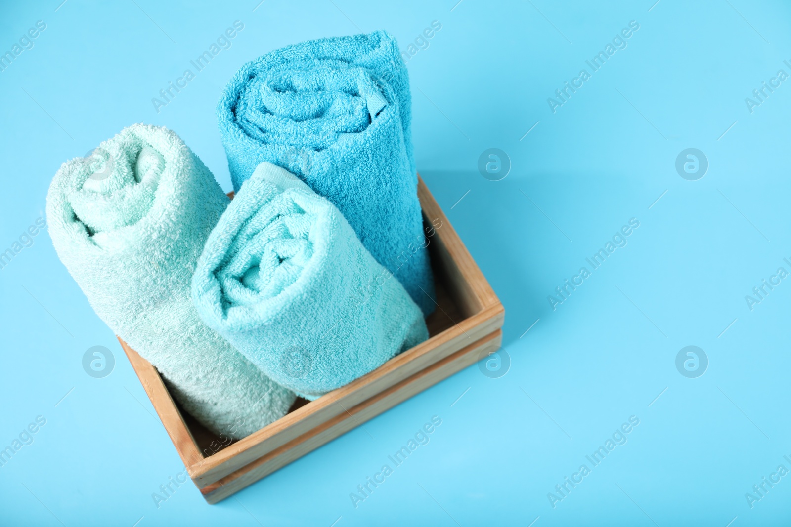Photo of Different soft towels in wooden basket on light blue background, above view. Space for text