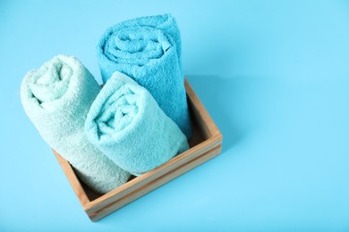 Photo of Different soft towels in wooden basket on light blue background, above view. Space for text
