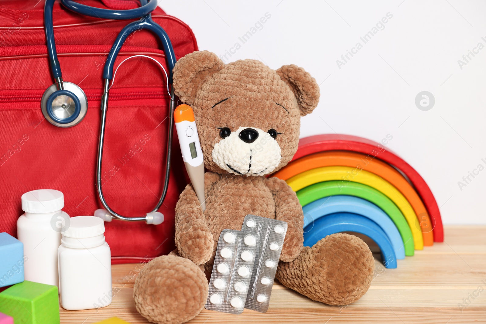 Pediatrician concept. Teddy bear, other toys, first aid, stethoscope, thermometer and pills on wooden table against white background, closeup Photo of Pediatrician concept. Teddy bear, other toys, first aid, stethoscope, thermometer and pills on wooden table against white background, closeup