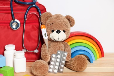 Photo of Pediatrician concept. Teddy bear, other toys, first aid, stethoscope, thermometer and pills on wooden table against white background, closeup