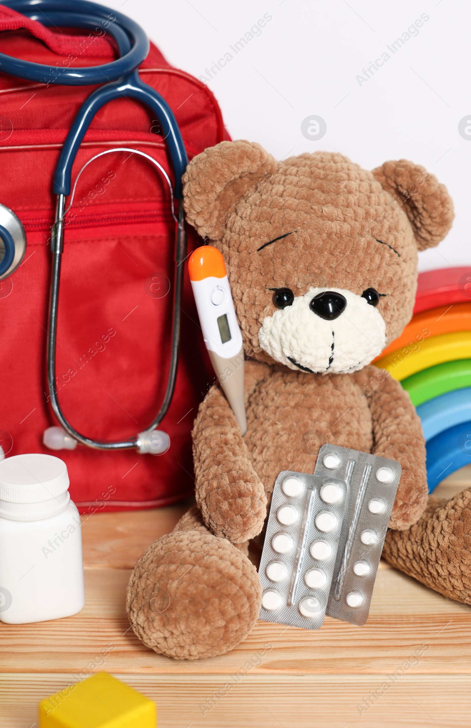 Pediatrician concept. Teddy bear, other toys, first aid, stethoscope, thermometer and pills on wooden table against white background, closeup Photo of Pediatrician concept. Teddy bear, other toys, first aid, stethoscope, thermometer and pills on wooden table against white background, closeup
