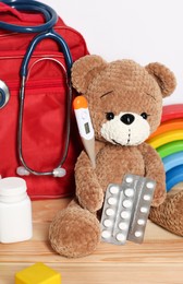 Photo of Pediatrician concept. Teddy bear, other toys, first aid, stethoscope, thermometer and pills on wooden table against white background, closeup