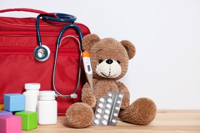 Photo of Pediatrician concept. Teddy bear, cubes, first aid, stethoscope, thermometer and pills on wooden table against white background