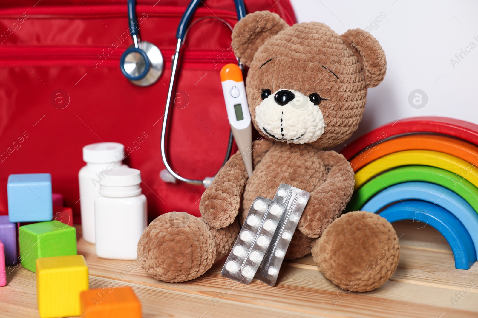 Pediatrician concept. Teddy bear, other toys, first aid, stethoscope, thermometer and pills on wooden table against white background, closeup Photo of Pediatrician concept. Teddy bear, other toys, first aid, stethoscope, thermometer and pills on wooden table against white background, closeup