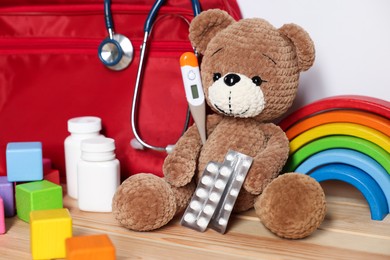 Photo of Pediatrician concept. Teddy bear, other toys, first aid, stethoscope, thermometer and pills on wooden table against white background, closeup