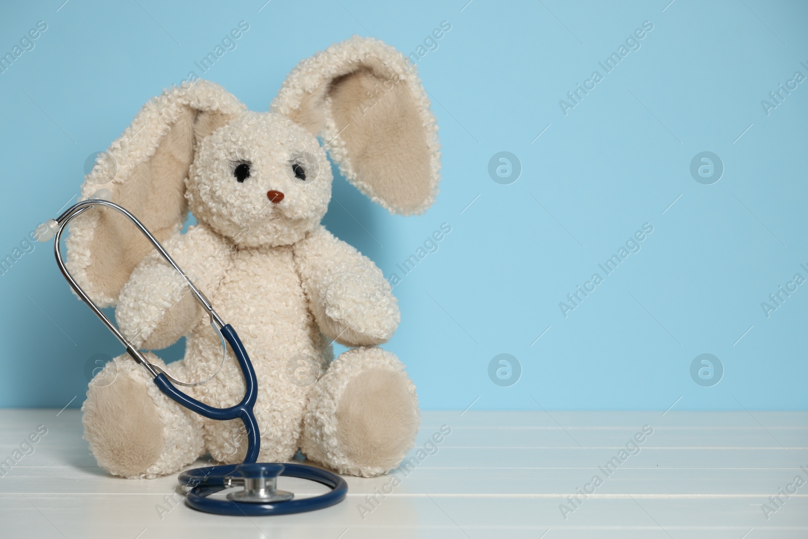 Pediatrician concept. Toy bunny and stethoscope on white wooden table against light blue background, space for text Photo of Pediatrician concept. Toy bunny and stethoscope on white wooden table against light blue background, space for text