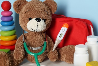Photo of Pediatrician concept. Toys, first aid kit, pills, thermometer and stethoscope on white wooden table against light blue background, closeup