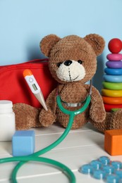 Photo of Pediatrician concept. Toys, first aid kit, pills, thermometer and stethoscope on white wooden table against light blue background, closeup