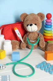 Photo of Pediatrician concept. Toys, first aid kit, pills, thermometer and stethoscope on white wooden table against light blue background, closeup