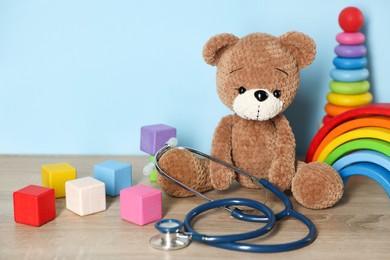 Photo of Pediatrician concept. Toys and stethoscope on wooden table against light blue background, closeup