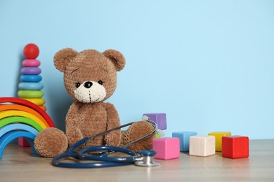 Photo of Pediatrician concept. Toys and stethoscope on wooden table against light blue background