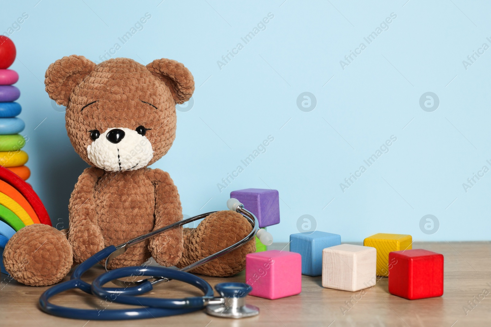 Pediatrician concept. Toys and stethoscope on wooden table against light blue background, closeup Photo of Pediatrician concept. Toys and stethoscope on wooden table against light blue background, closeup