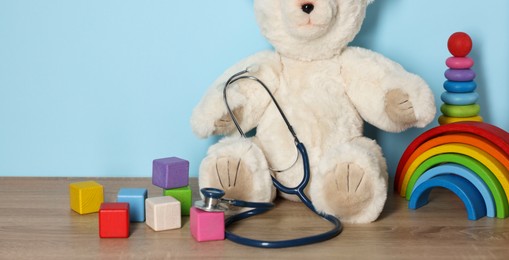 Photo of Pediatrician concept. Toys and stethoscope on wooden table against light blue background