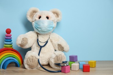 Photo of Pediatrician concept. Toys, medical mask and stethoscope on wooden table against light blue background, space for text