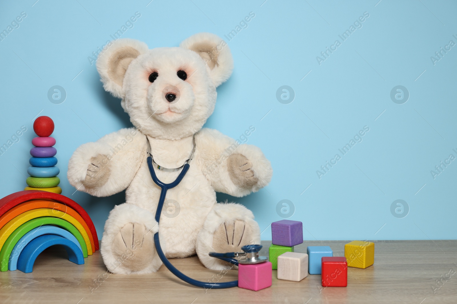 Pediatrician concept. Toys and stethoscope on wooden table against light blue background, space for text Photo of Pediatrician concept. Toys and stethoscope on wooden table against light blue background, space for text