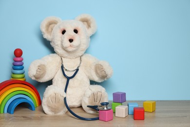 Photo of Pediatrician concept. Toys and stethoscope on wooden table against light blue background, space for text