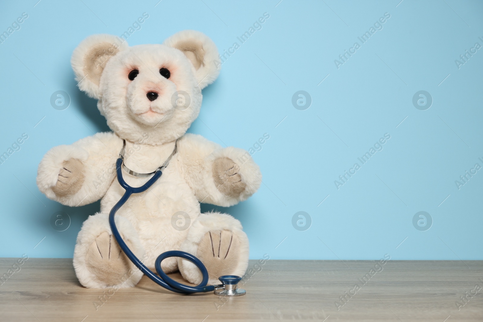 Photo of Pediatrician concept. Toy bear and stethoscope on wooden table against light blue background, space for text