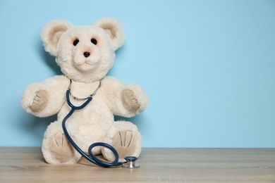 Photo of Pediatrician concept. Toy bear and stethoscope on wooden table against light blue background, space for text