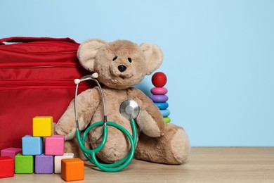 Photo of Pediatrician concept. Toys, stethoscope and first aid kit on wooden table against light blue background, space for text