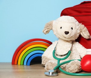 Photo of Pediatrician concept. Toys, stethoscope and first aid kit on wooden table against light blue background, closeup