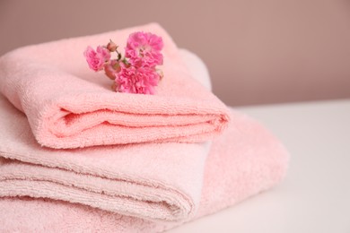Photo of Stack of soft towels and flowers on white table, closeup. Space for text