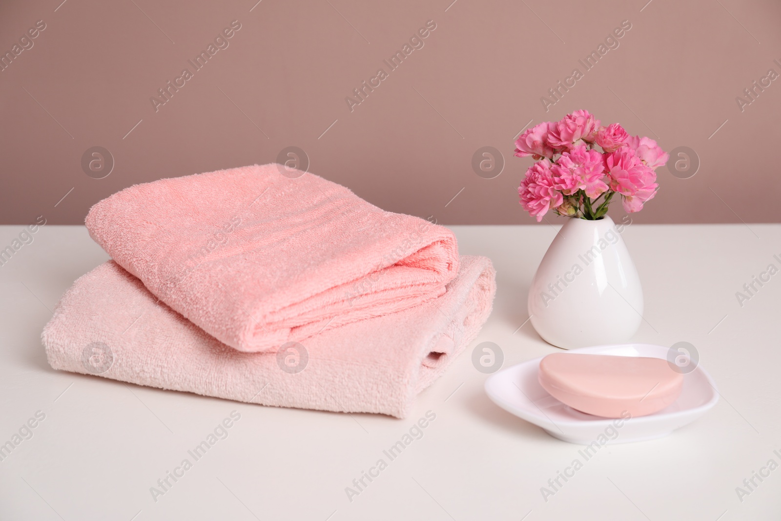 Photo of Stack of soft towels, flowers and soap on white table