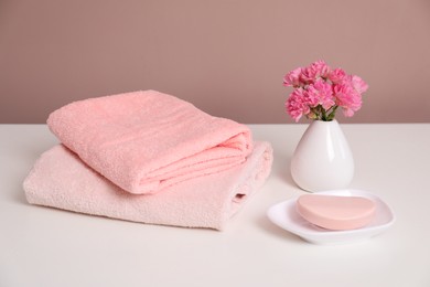 Photo of Stack of soft towels, flowers and soap on white table
