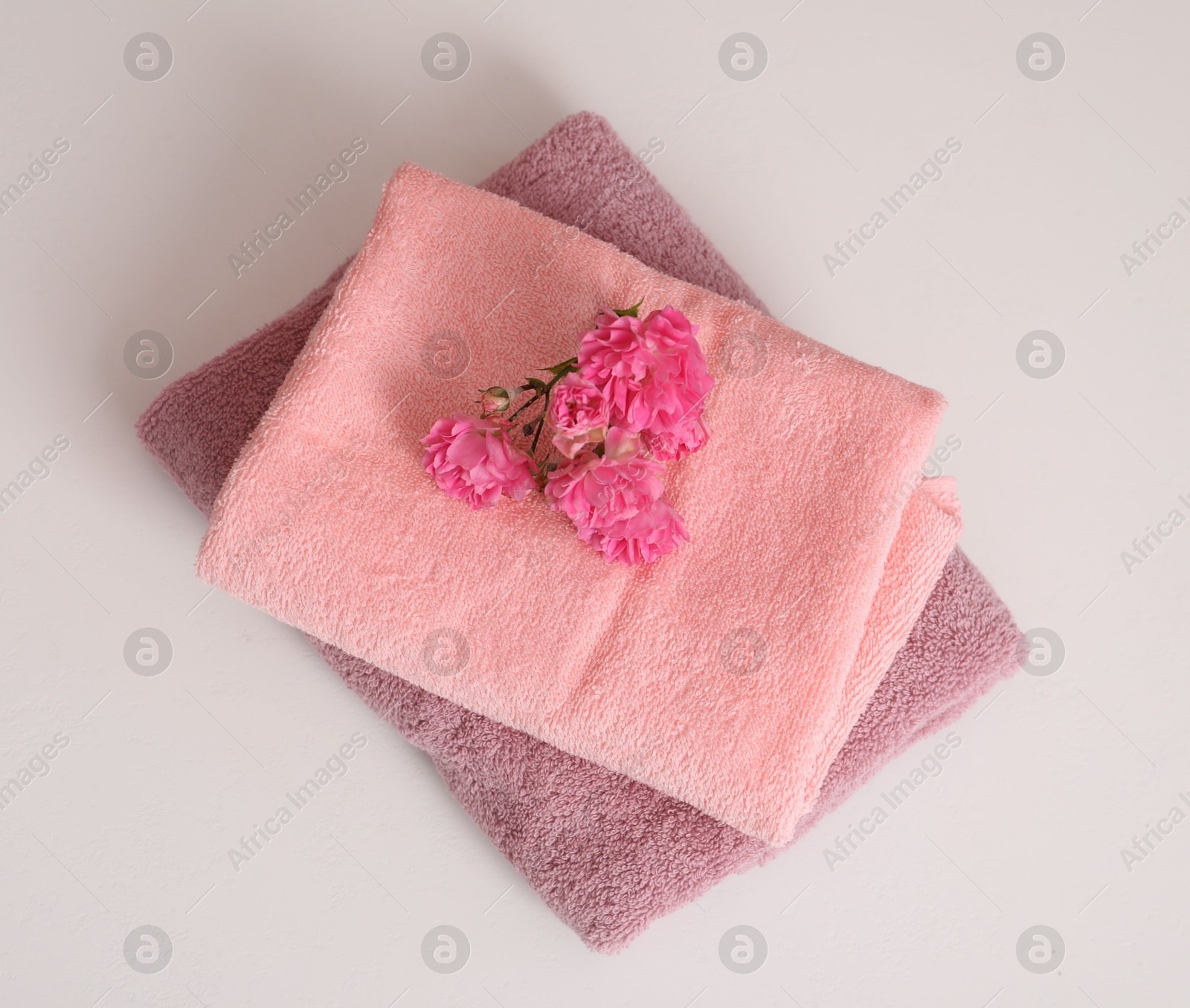 Photo of Stack of colorful towels and flowers on white table, top view