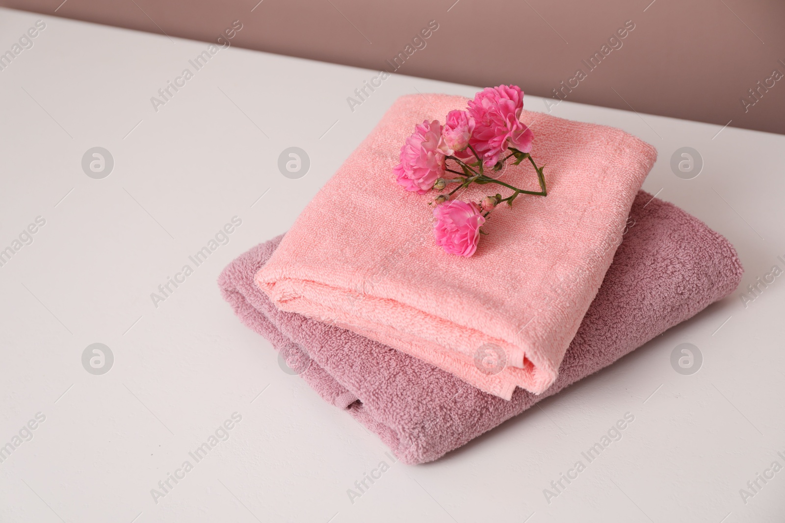 Photo of Stack of colorful towels and flowers on white table, space for text