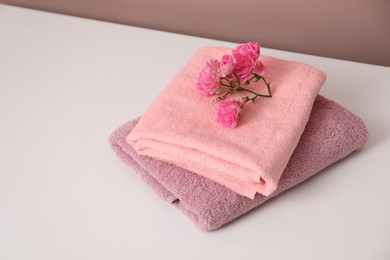 Photo of Stack of colorful towels and flowers on white table, space for text